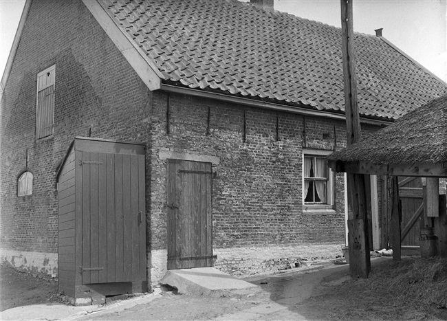 Boerderij met een woon- en een stalgedeelte. Links tegen de gevel een buitentoilet en rechts een hooiberg.