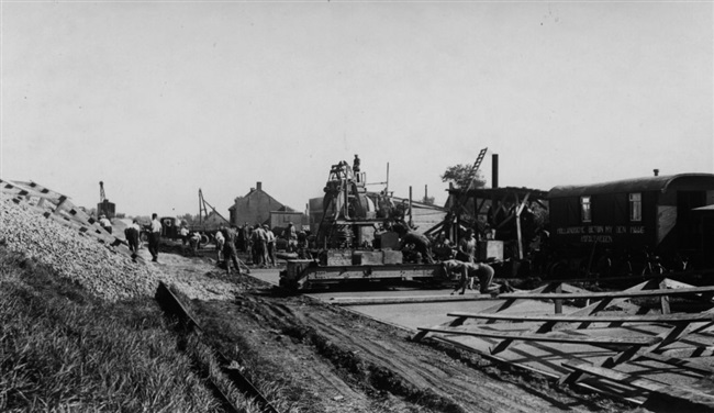 De Provinciale Waterstaat verbetert de weg onderaan de dijk tussen Maassluis en Hoek van Holland. Deze weg loopt evenwijdig aan de provinciale weg, de huidige N220/Maasdijk. Het stuk weg op de voorgrond is klaar. De foto is waarschijnlijk gemaakt in de buurt van Maasdijk.