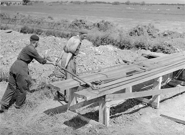Aanleg van de weg op palen tussen Boskoop en Alphen aan den Rijn. IJzervlechters buigen het ijzer voor de wapening van de dwarsbalken. Op de dwarsbalken komt later het wegdek te rusten.