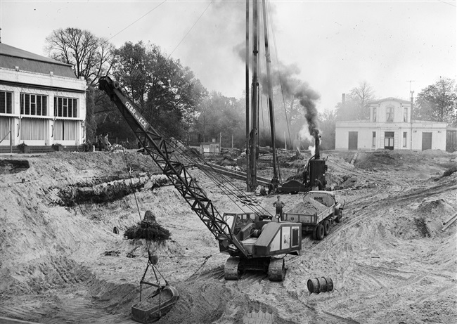Heiwerkzaamheden voor de bouw van de hoogbouw, van het nieuwe provinciehuis. Op de achtergrond het voormalige directiegebouw van de Haagsche Dierentuin.