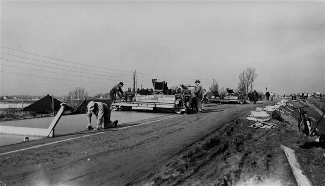 De Provinciale Waterstaat verbetert de provinciale weg tussen Maassluis en Hoek van Holland, de huidige N220/Maasdijk. De Gebr. Hogenbirk uit Laren leggen het betonnen wegdek machinaal aan op de dijk. Deze foto is gemaakt in de buurt van Maasdijk.
