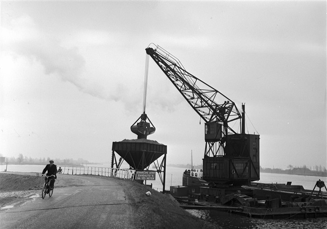 Uit een binnenvaartschip wordt zand overgeladen in een tijdelijke opslag. Het zand wordt gebruikt voor de aanleg van de (drijvende) weg nr. 29 tussen Gouda, Stolwijk en Bergstoepseveer.