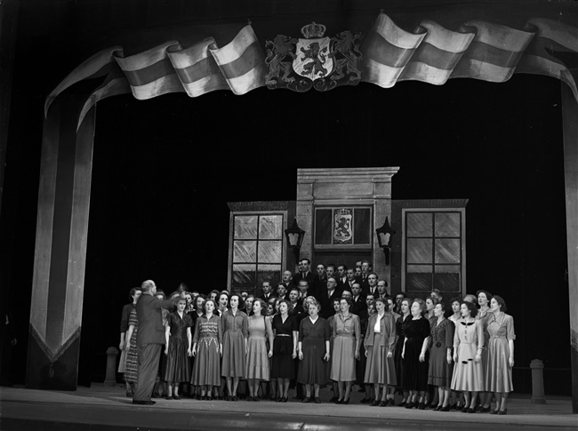 Provincieambtenaren repeteren 'Het lied van Zuid-Holland' in de Koninklijke Schouwburg, ter gelegenheid van het bezoek van het koninklijk paar aan Den Haag op 16 november.
