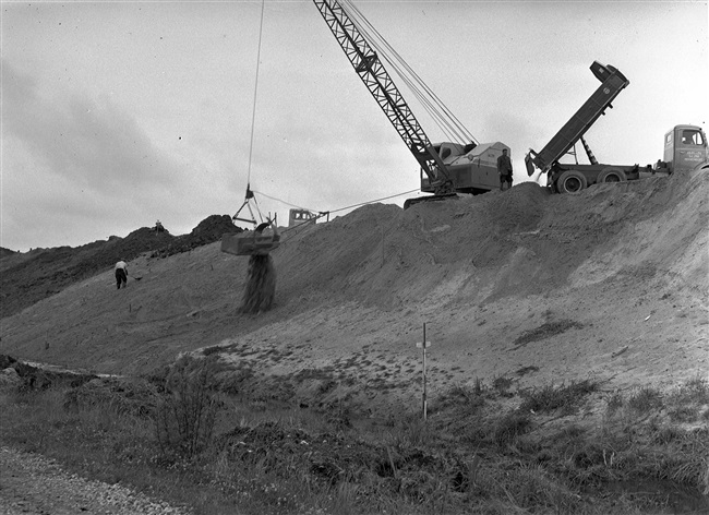 Dijkbouw. Met een dragline wordt het dijkprofiel afgewerkt.