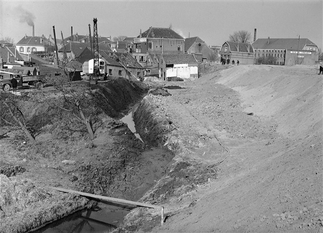 Oorspronkelijke titel 'verzakking dijk'. Waarschijnlijk wordt hier de aansluiting van de nieuwe weg, de N207, tussen Gouda, Stolwijk en Bergambacht voorbereid. Rechts het kaaspakhuis van Gebr. De Vreugt.