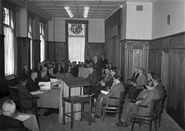 Openbare vergadering van de Gedeputeerde Staten in Den Haag. Het Haagsche Taxi vraagstuk wordt behandeld aan het Korte Voorhout 1. Links aan tafel zitten o.a. griffier mr. F.A. Helmstrijd en gedeputeerde mr. H. van Riel.