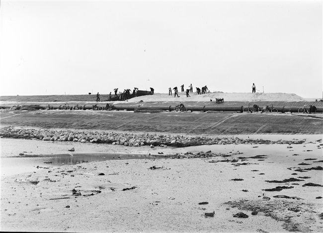 Dijkherstel bij Oude-Tonge na de watersnoodramp van 1 februari 1953. Het nieuwe dijklichaam van opgespoten zand wordt bekleed met zandasfalt.