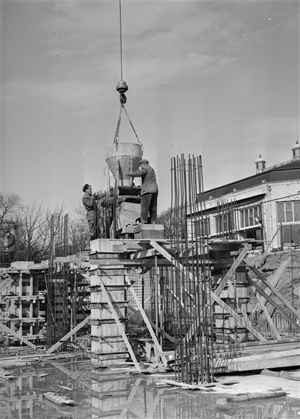 Betonstorters storten met een betonkubel de betonkolommen van het nieuwe provinciehuis. Rechts het restaurant van de voormalige Haagsche Dierentuin.