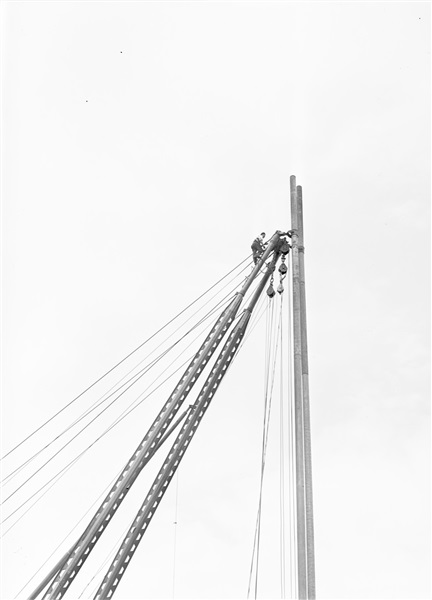 Aanleg van de weg op palen tussen Boskoop en Alphen aan den Rijn. Een man die naar boven is gehesen ontwart de kabels van een heistelling.