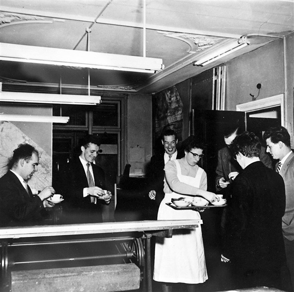 Kantoor van de Provinciale Waterstaat in Den Haag. Een kantinemedewerker voorziet ambtenaren van koffie en thee. De foto is gemaakt tussen 1950 en 1969.