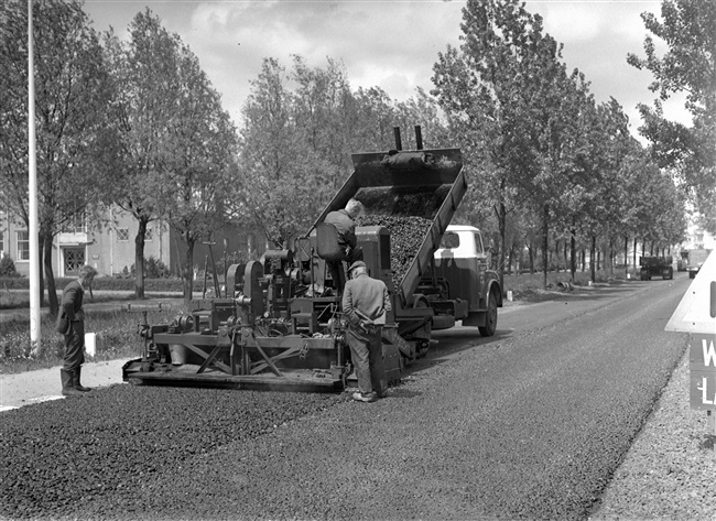 Verbetering van de Tiendweg. Met een Barber-Greene asfaltmachine wordt op de fundering van gewalst puin een deklaag aangebracht van grof asfaltbeton.