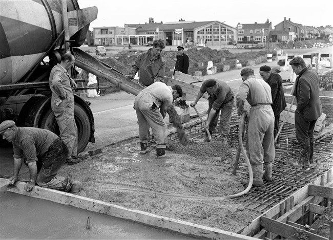 Een kruising in de Tiendweg wordt verbeterd. Een betonstorter stort beton in de wapening voor het wegdek. Met een pneumatische vibrator wordt het beton vervolgens aangetrild.
