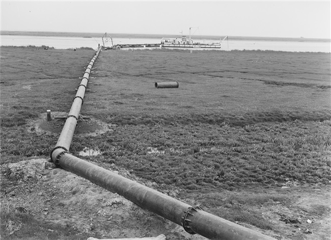 De dijk bij Stellendam wordt hersteld na de watersnoodramp van 1 februari 1953. Zand en water worden via een buis geperst naar de plek waar een nieuw dijklichaam wordt opgespoten.