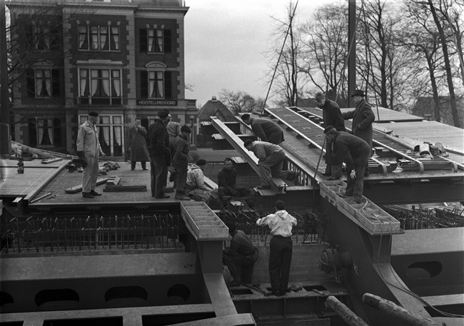 De Oude Tolbrug over het Rijn-Schiekanaal, beter bekend als de Vliet, wordt vervangen door een basculebrug. Monteurs monteren de bovenbouw van de nieuwe brug. Op de achtergrond villa Dorrepaal, het vroegere Huize Leeuwenbergh aan de Westvlietweg.