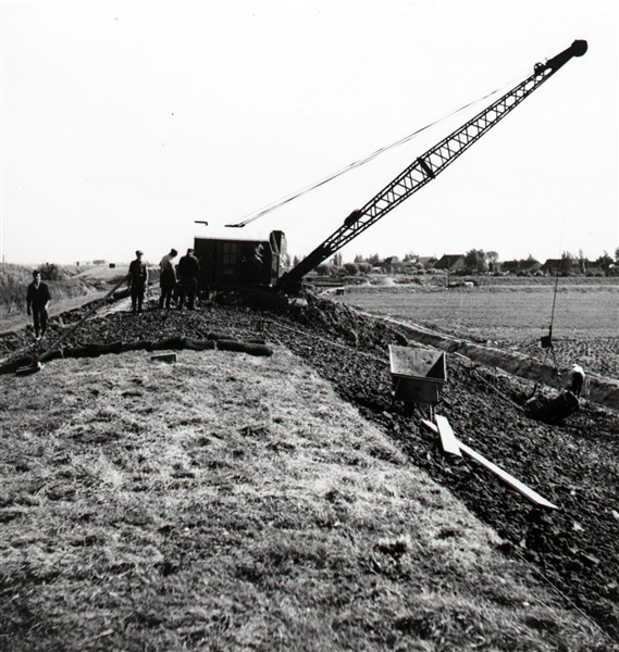 Dijkverzwaring, waarbij een dijk wordt verhoogd en verbreed. Een dragline, of draadkraan, verplaatst de grond uit de sloot naar de dijk. De foto is waarschijnlijk gemaakt tussen 1950 en 1960.