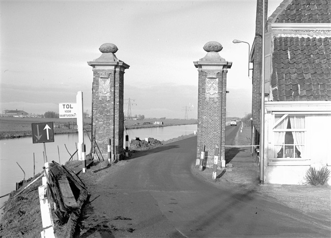 De Tertiaire weg T2 richting Voorhout bij het tolhuis met tolpoort aan de Haarlemmertrekvaart. De weg was onderdeel van het Tertiair Wegenplan in de provincie Zuid-Holland. De poort bevat de wapens van Haarlem en Leiden.