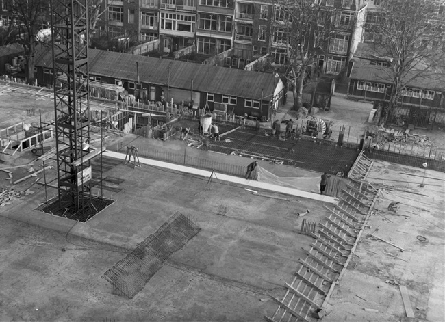 De vloeren van het hoofdgebouw (huidige gebouw C) worden gestort. In dit gedeelte van het provinciehuis komen o.a. de Statenzaal en de entreehal. Links op de achtergrond de lange keet van de aannemer en rechts de bouwkeet van de bouwdirectie en de tekenkamer.