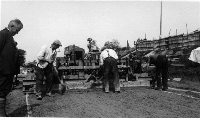 De Provinciale Waterstaat verbetert de weg onderaan de dijk tussen Maassluis en Hoek van Holland. Deze weg loopt evenwijdig aan de provinciale weg, de huidige N220/Maasdijk. Een stampmachine verdicht het grindbeton. De foto is waarschijnlijk gemaakt in de buurt van Maasdijk.