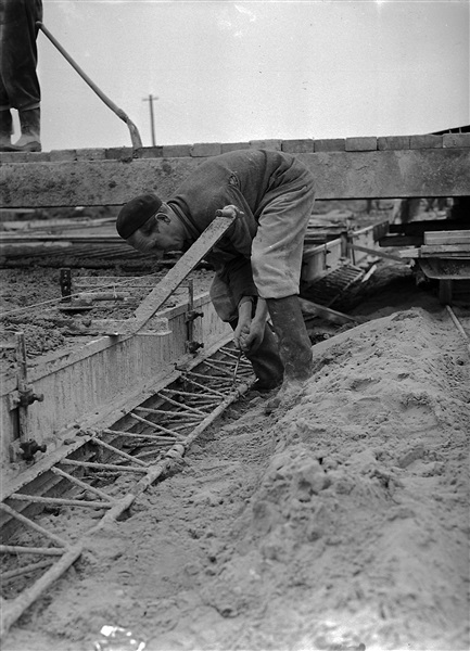 Aanleg van de weg op palen tussen Boskoop en Alphen aan den Rijn door de Provinciale Waterstaat. Achter de man wordt vanaf een verrijdbare vlonder het beton gestort in de wapening.