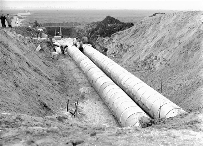 Dijkaanleg. Voor een goede afwatering van de polders worden door de dijk enkele duikers aangebracht. De hiervoor gebruikte Aramko-buizen monteert men op een werkvloer van houtvezelbalen.