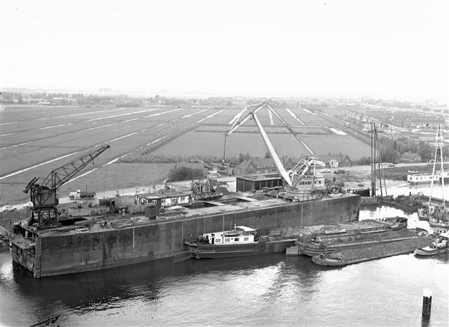 Aanleg van een weg op zandpalen. Met een grijper wordt het per schip aangevoerde zand in een silo gestort en vervolgens met zandauto's afgevoerd.