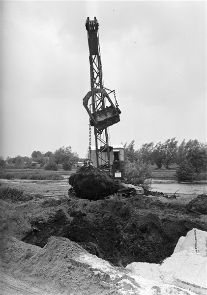 Aanleg van de drijvende weg, provinciale weg nr. 30, tussen Bergambacht en Schoonhoven. Voor het verstevigen van de natte ondergrond worden houtvezelbalen (rechts) gebruikt, om verzakking van de wegverharding tegen te gaan.