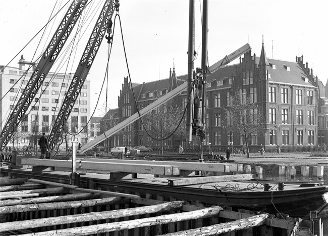 Aanvoer van heipalen voor de bouw van de eerste St. Sebastiaansbrug. Rechts het voormalige laboratorium van de Afdeling Physica en Electrotechniek van de Polytechnische School.
